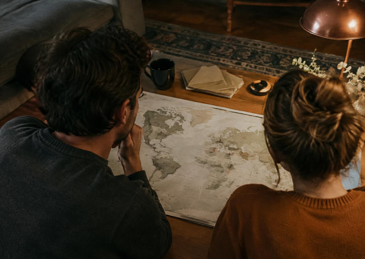 A couple leans over a world map with marked places in the evening.